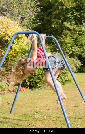 Trois ans, fille, faisant de l'acrobatie sur appareil de gymnastique dans le jardin arrière pour jouer, au Royaume-Uni. Banque D'Images