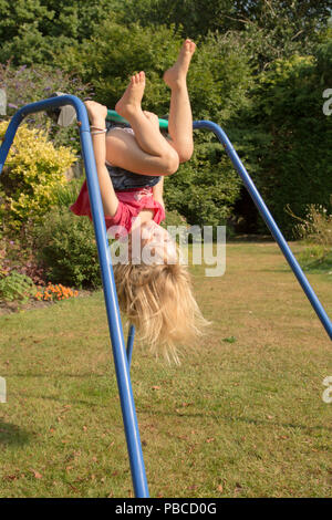 Trois ans, fille, faisant de l'acrobatie sur appareil de gymnastique dans le jardin arrière pour jouer, au Royaume-Uni. Banque D'Images