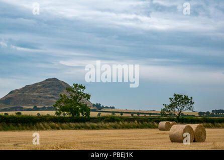 East Lothian, Ecosse, Royaume-Uni, le 28 juillet 2018. Météo France : nuages sombres se rassemblent avec un ciel menaçant d'orage sur Berwick law récemment récoltés avec pelouse avec des balles de foin rondes Banque D'Images