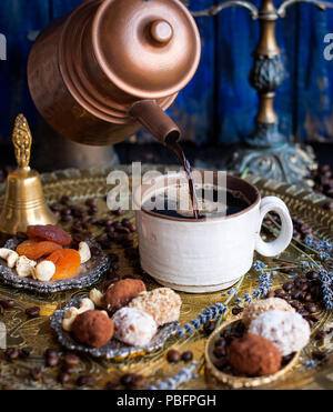 La cafetière se verse le café dans la tasse. dans un style oriental. bonbons artisanaux, fruits secs et de fleurs. dans le style d'art de l'obscurité. et de la céramique. Banque D'Images