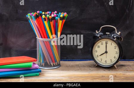 De temps pour l'école. Les fournitures scolaires et réveil sur un bureau en bois, blackboard background Banque D'Images
