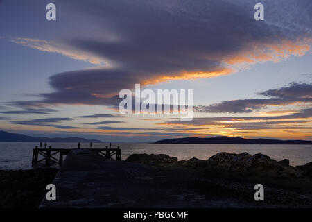 Ancienne jetée à Portencross Seamill en Écosse avec cinq personnes dans silhoutte of mountain range at sunset la pêche au large de la jetée au coucher du soleil avec de beaux nuages et un ciel de coucher du soleil. Banque D'Images