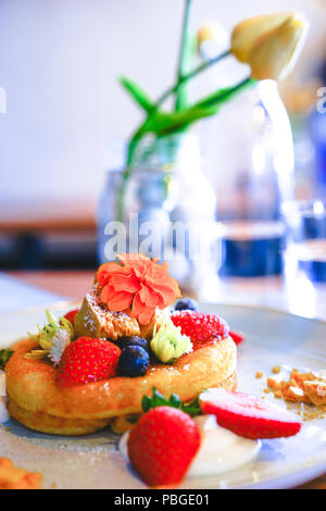 Hot pan cake garni de fraises fraîches , myrtilles, miel et des fleurs pour la décoration sur le plat blanc Banque D'Images