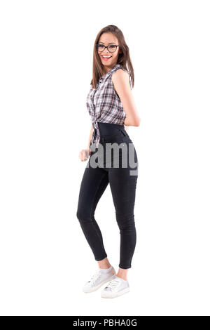 Une belle jeune femme en chemise à carreaux smiling at camera posant avec main derrière l'arrière. Corps plein isolé sur fond blanc. Banque D'Images