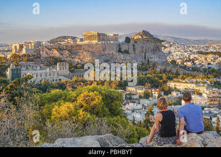 Couple regard la merveilleuse vue de la colline Filopappou en regardant vers l'acropole d'Athènes au coucher du soleil. L'Attique, la Grèce, l'Europe. Banque D'Images