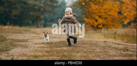 Enfant fille court, s'amuse et joue avec son chien au cours de marche en forêt d'automne. Banque D'Images