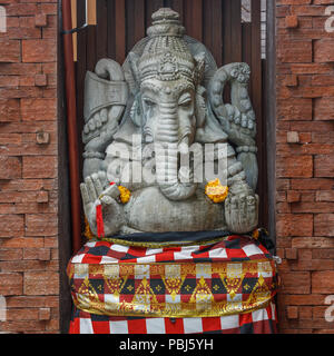 Statue de Ganesh hindou en pierre en sarong, décoré de fleurs de souci. Bali, Indonésie. Banque D'Images