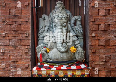 Statue de Ganesh hindou en pierre en sarong, décoré de fleurs de souci. Bali, Indonésie. Banque D'Images