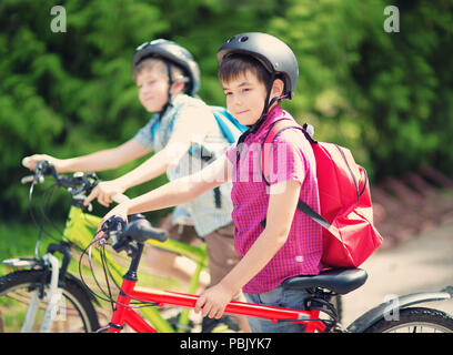 Les enfants avec des sacs à dos équitation sur des vélos dans le parc près de l'école Banque D'Images