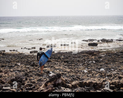 Playa de Las Americas, Tenerife, Espagne - 10 juillet 2018 : Surfer walking de passage sur les rochers vers la mer à la plage de Las Americas Banque D'Images