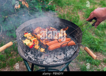 Griller les saucisses, les ailes de poulet et shashlicks sur la grille du barbecue. Banque D'Images