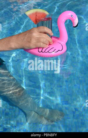 Woman's hand holding millénaire une boisson froide dans un flamant rose porte-boissons flottant dans une piscine Banque D'Images