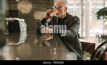 Mid adult businessman sitting at a cafe boire du café et à l'aide de smart phone. En couple à la recherche d'écouteurs à son portable dans un café. Banque D'Images