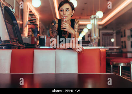 Femme aux mains tatouées de boire une boisson avec une paille dans un restaurant. Happy woman standing in a cafe boire une boisson gazeuse à la route.