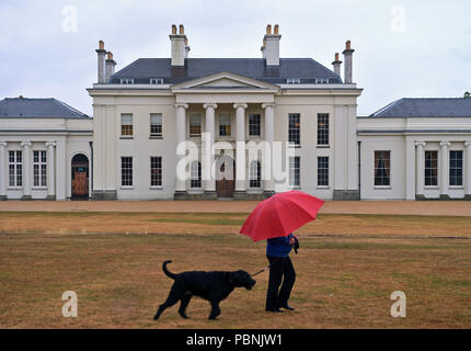 Une femme entre son chien passé Hylands House à Hylands Park à Chelmsford, Essex, que des pluies violentes et des rafales allant jusqu'à 50 mph vu le week-end d'affouillement continuer après des semaines de temps sec et chaud. Banque D'Images