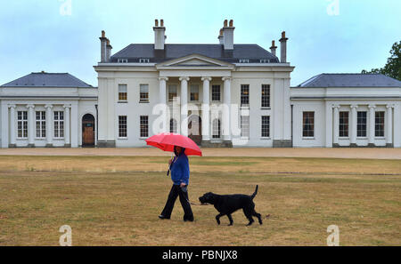 Une femme entre son chien passé Hylands House à Hylands Park à Chelmsford, Essex, que des pluies violentes et des rafales allant jusqu'à 50 mph vu le week-end d'affouillement continuer après des semaines de temps sec et chaud. Banque D'Images