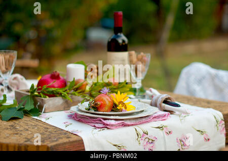 Le déjeuner est romantique dans le jardin d'automne, atmosphère de vacances et de confort. Dîner d'automne en plein air avec vin et fruits. Table de décoration avec fleurs et grenade. Photo vintage Banque D'Images