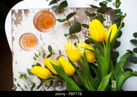 Tulipes jaunes sur un tableau blanc avec des verres de vin rose Banque D'Images