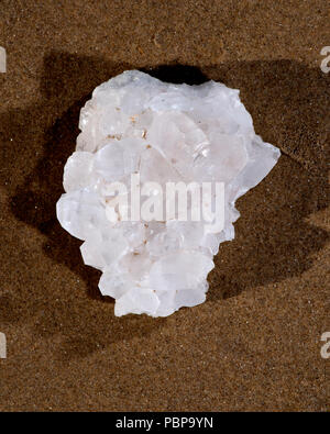 Cluster de quartz clair de l'Himalaya avec inclusions d'hématite sur du sable mouillé sur la plage au lever du soleil. Banque D'Images