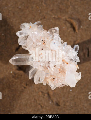 Cluster de quartz clair de l'Himalaya avec inclusions d'hématite sur du sable mouillé sur la plage au lever du soleil. Banque D'Images