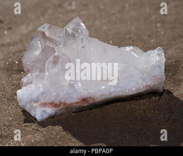 Cluster de quartz clair de l'Himalaya avec inclusions d'hématite sur du sable mouillé sur la plage au lever du soleil. Banque D'Images