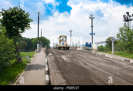 Niveleuse jaune de la conduite sur la route asphaltée à l'été Banque D'Images