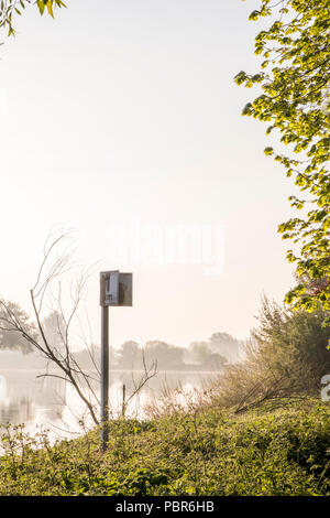 Dawn scène Riverside. Arbres et un kilomètre marqueur de distance sur une rivière sur un matin de printemps brumeux sur la rivière Trent, Lancashire, England, UK Banque D'Images