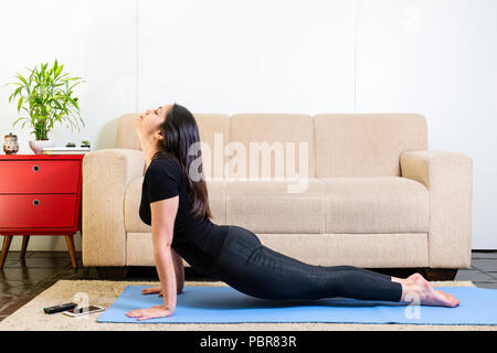 Belle femme brunette caucasien de noir sur bleu yogamat faisant face vers le haut-chien posent Banque D'Images