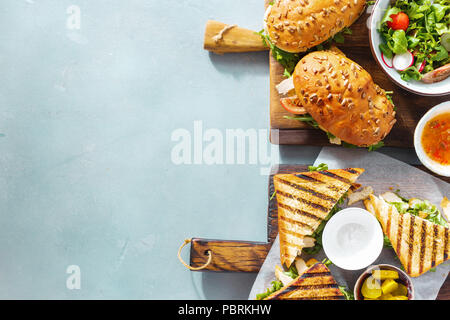 Sandwich grillé avec des pépites, salade, sauce et concombres sur fond bleu avec copie espace, vue du dessus. Divers en-cas. Concept alimentaire en plein air Banque D'Images