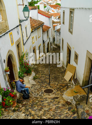 Homme plus âgé assis sur la marche avant d'une maison dans une rue très étroite et escarpée de Castelo de vide Alentejo Portugal Banque D'Images