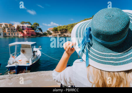 Happy young woman holding straw hat profiter de vacances à Assos village en face de la baie d'émeraude de la Méditerranée bateau blanc et de belles maisons traditionnelles de Céphalonie, Grèce Banque D'Images