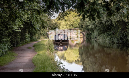 Une scène paisible à la recherche vers le bas d'un canal de halage. Il y a un petit bateau amarré devant une vieille route pont traversant l'eau.. La scène se passe je Banque D'Images