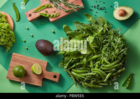 Gren légumes pour salade - laitue, pois verts, bâtons, Rosemary, avocat, la chaux sur une planche à découper en bois sur un fond vert deux tons. Vue d'en haut Banque D'Images