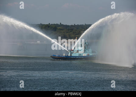 Un remorqueur incendie pulvériser de l'eau de lutte contre l'incendie il est puissant flexibles dans le port de Southampton docks près de fawley esso raffinerie de pétrole. Banque D'Images