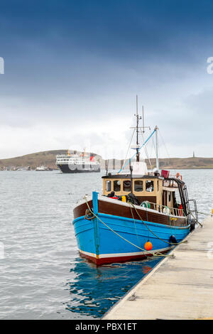 Un petit bateau de pêche amarré près de la jetée du Nord comme une CalMac ferry îles périphériques 'Isle of Lewis' arrive à Oban, Argyll and Bute, Ecosse, Royaume-Uni Banque D'Images