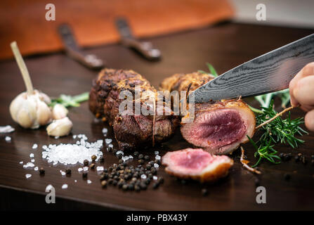 Découper une portion de rôti de bœuf biologique rouleau avec couteau sur table en bois avec de l'ail Sel et poivre à Melbourne, Australie Banque D'Images