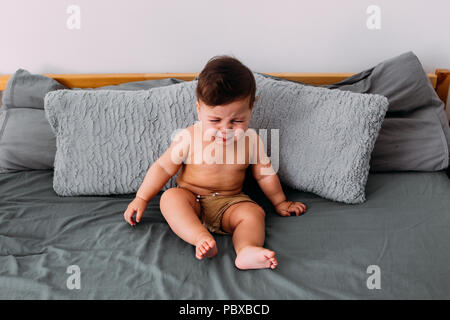 Bébé qui pleure ennuyé assis sur le lit de la chambre portant des shorts, de frustration concept Banque D'Images