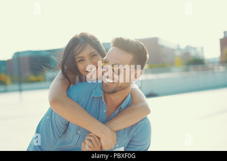 Happy young woman embracing man élégant de l'arrière à l'extérieur dans le coucher du soleil, piggyback ride Banque D'Images