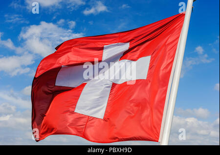 Le drapeau suisse est forme dans le vent contre un ciel bleu avec des nuages Banque D'Images