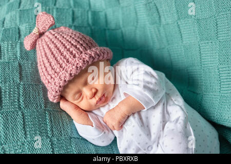 Mignon bébé nouveau-né dort dans un chapeau. Vêtements en laine vert arrière-plan. Banque D'Images