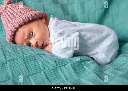 Nouveau-né bébé fille surpris au lit. Vêtements chauds d'hiver, bonnet de laine rose. Banque D'Images