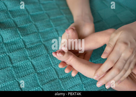 Les jambes du nouveau-né dans les mains de la mère. En laine chaude couverture verte. Banque D'Images