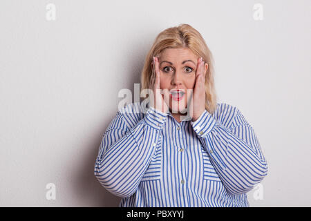 Portrait d'une femme en surpoids peur en studio, les mains sur les joues. Banque D'Images