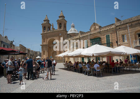 Les visiteurs du marché du dimanche de Marsaxlokk faites une pause dans un des nombreux restaurants de la ville. Ils sont négligés par l'église paroissiale. Banque D'Images