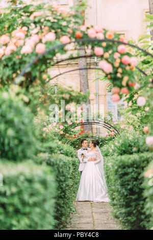 Sur toute la longueur de la cheerful jeunes mariés passer du temps dans le beau jardin de roses. Banque D'Images