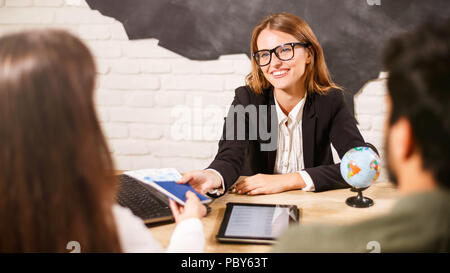 Belle femme agent de voyage à lunettes est la collaboration avec les clients en leur offrant des tours et de bureau Banque D'Images