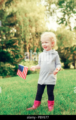 Heureux adorable petit blond Caucasian girl smiling holding rire et brandissant un drapeau américain à l'extérieur de célébrer le 4 juillet, jour de l'indépendance, d'un drapeau Da Banque D'Images