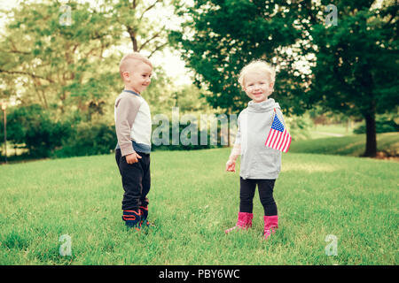 Heureux adorable petit blond Caucasian girl and boy smiling rire tenant la main et en agitant le drapeau américain à l'extérieur de célébrer le 4 juillet, Independenc Banque D'Images