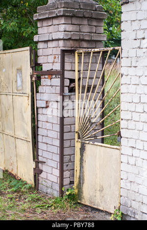 Ancienne grille rouillée et branlante guichet jaune métal avec une serrure entre les deux piliers en brique. Banque D'Images