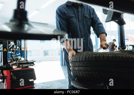 Pneu de voiture mécanicien supprime station-service. L'homme d'intervenir sur la machine de dépose en caoutchouc de la roue. Banque D'Images